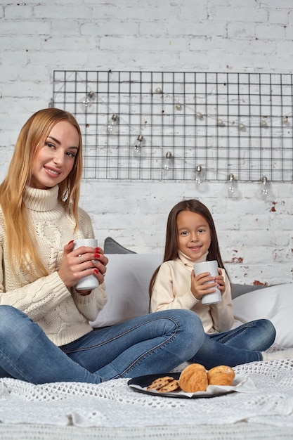Moeder en dochter drinken thee of cacao uit grote mokken die op bed staan