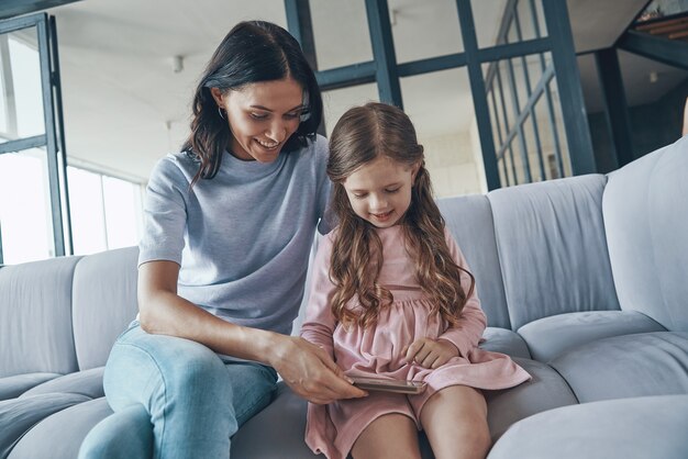 Moeder en dochter gebruiken smartphone terwijl ze thuis op de bank zitten