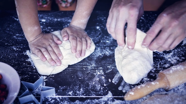 Moeder en dochter handen kneden deeg op een houten tafel. Bakken voorbereiden