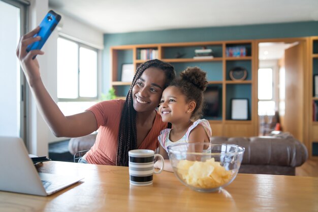 Moeder en dochter hebben samen plezier en nemen een selfie met mobiele telefoon terwijl ze thuis blijven. monoparentaal concept.