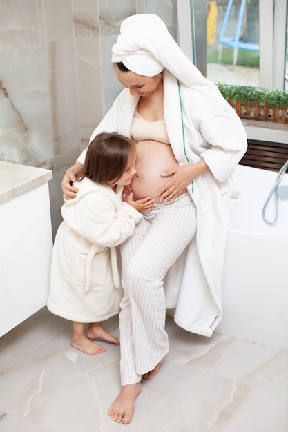 Moeder en dochter in de ochtend in de badkamer Babymeisje in een witte badjas knuffelt haar moeder