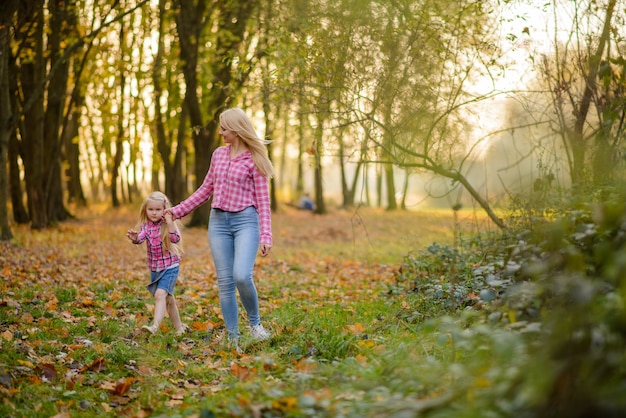 Moeder en dochter in jeans en roze shirts lopen in de herfst park.