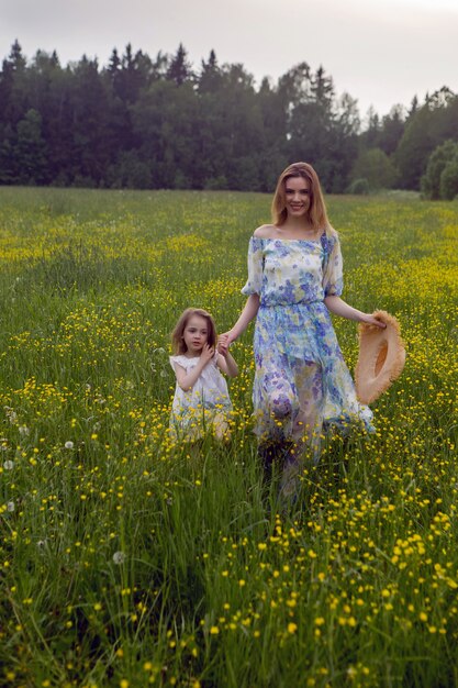 Moeder en dochter in jurken en een hoedentribune in een veld met gele bloemen in de zomerdag