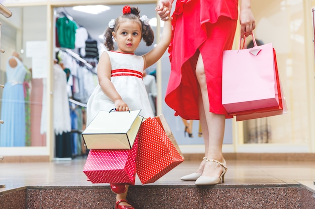 Moeder en dochter in jurken in het winkelcentrum met kleurrijke tassen