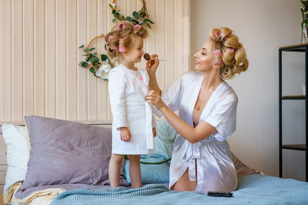 Moeder en dochter in krulspelden, maken een make-up aan elkaar, een gelukkig gezin