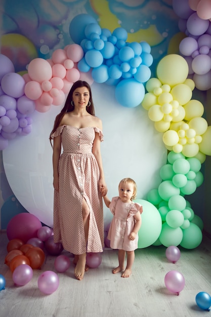 Moeder en dochter in roze jurken staan op een witte achtergrond met kleurrijke ballonnen