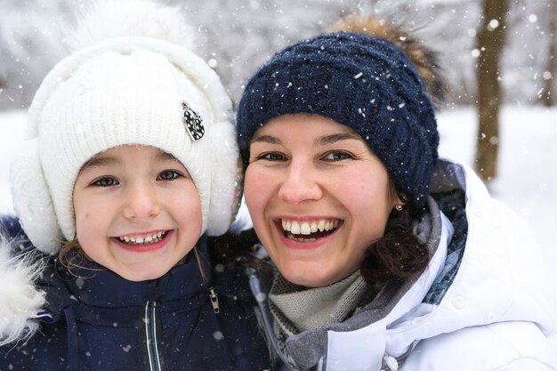 Moeder en dochter in warme kleren in het besneeuwde bos knuffelen en kijken. kerstvakantie