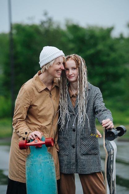 Moeder en dochter knuffelen, leunend op skateboards op een regenachtige dag