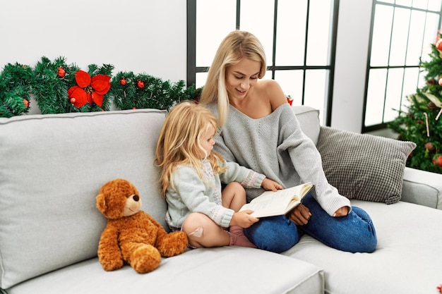 Moeder en dochter leesboek zittend bij de kerstboom thuis