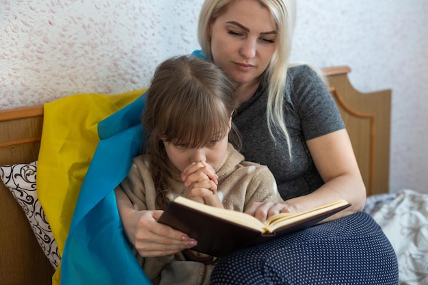 Moeder en dochter lezen een boek met de vlag van Oekraïne in bed