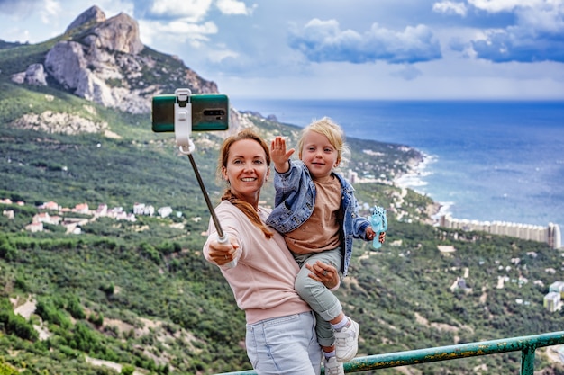 Foto moeder en dochter maken een selfie op de achtergrond van uitstekende bergen, wolken en de zee de conc...