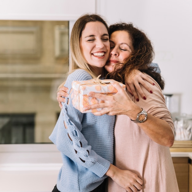 Foto moeder en dochter met cadeau knuffelen in de keuken