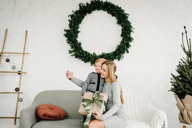 Foto moeder en dochter met cadeautjes worden gefotografeerd aan de telefoon in de buurt van de kerstboom