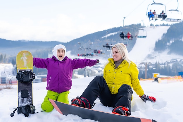 Moeder en dochter met snowboards spelen in de sneeuw