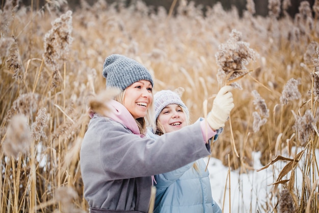 Moeder en dochter op een wandeling in het bos, gras en sneeuw, winterwandelingen, bos, veld, winterkleren