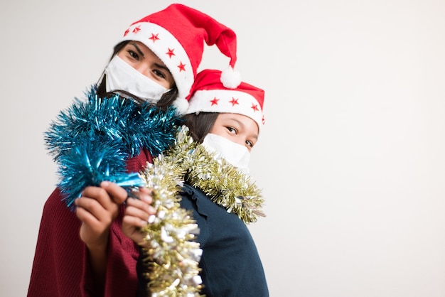 Moeder en dochter op zoek naar de camera met kerstmuts en chirurgisch masker met klatergoud fonkelde op witte achtergrond.