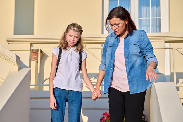 Moeder en dochter schoolmeisje met een rugzak op de veranda van het huis