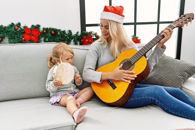 Moeder en dochter spelen gitaar en tamboerijn zitten bij kerstdecor thuis