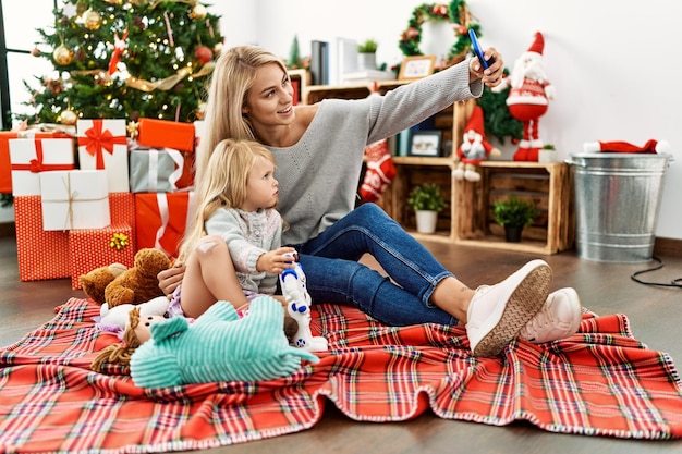 Moeder en dochter spelen met speelgoed en maken selfie door de smartphone die thuis bij de kerstboom zit