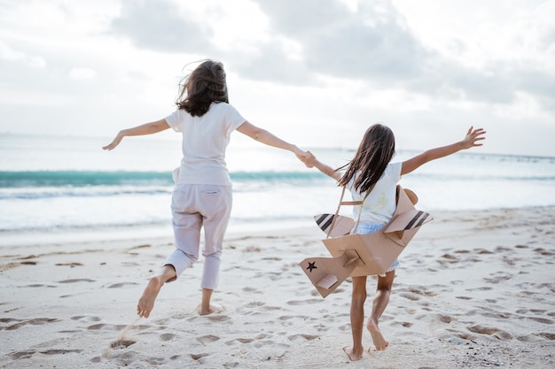 Moeder en dochter spelen samen met kartonnen vliegtuig op het strand