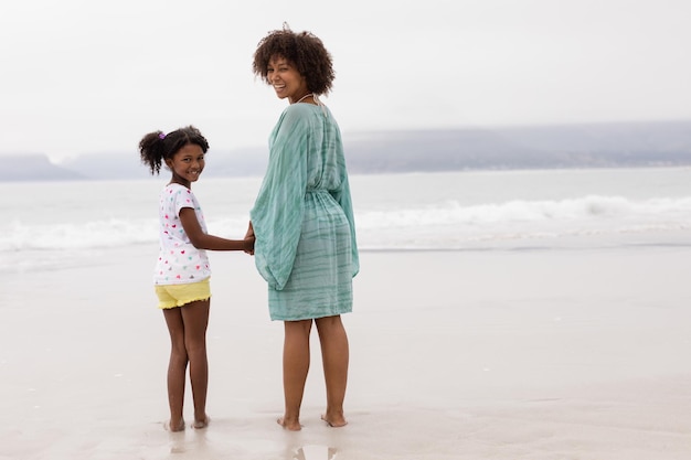 Moeder en dochter staan hand in hand op het strand.