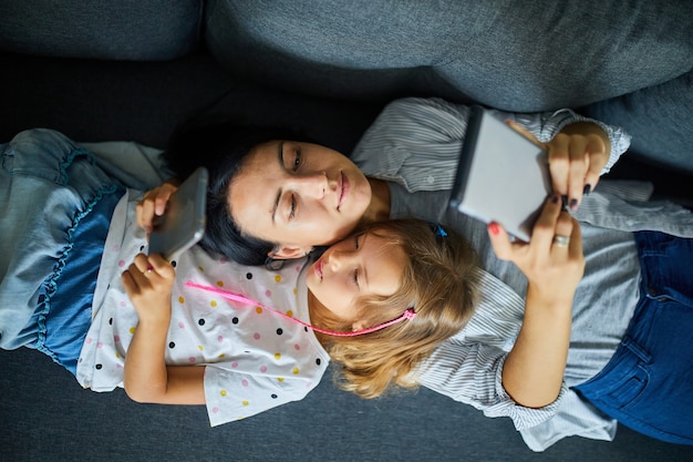 Moeder en dochter surfen op mobiele telefoon terwijl ze samen ontspannen op de bank thuis