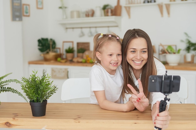 Moeder en dochter tonen vredesgebaar naar de camera. Een blog schrijven naar een videoplatform.