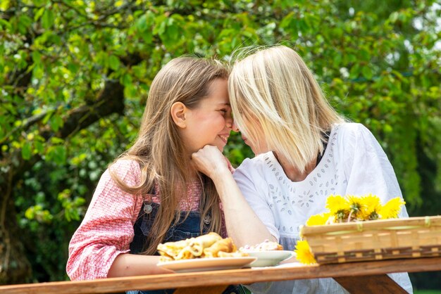 Moeder en dochter van negen jaar zitten omhelzend aan een tafel in de tuin