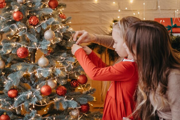 Moeder en dochter versieren samen de kerstboom. traditioneel ouderschap.