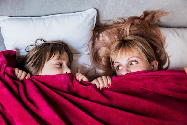 Moeder en dochter verstoppen zich onder een deken in een bed thuis. Boven weergave