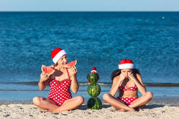 Moeder en dochter vieren zomerkerstmis op het strand en eten watermeloen