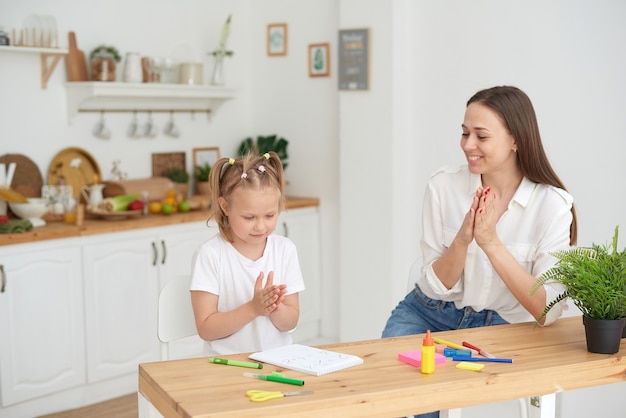 Moeder en dochter zijn klaar met hun huiswerk, verheugen zich en klappen in hun handen. Het concept van het zorgen voor een kind en helpen met huiswerk.