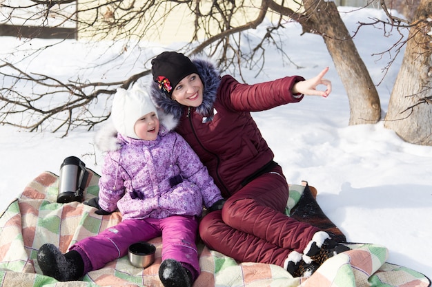 Moeder en dochter zitten in de winter op een plaid in de sneeuw.