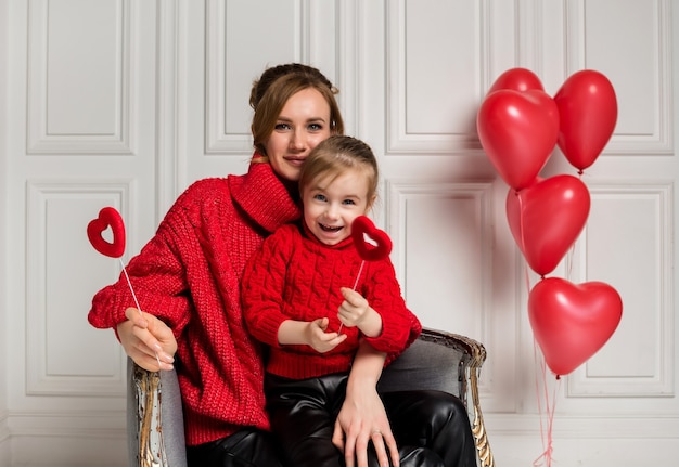 Moeder en dochter zitten in een stoel en houden rode harten op stok op wit