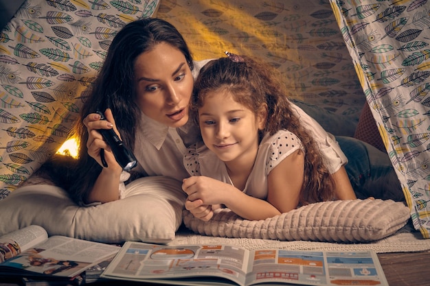 Moeder en dochter zitten in een tipi-tent verhalen te lezen met de zaklamp. Gelukkig gezin.