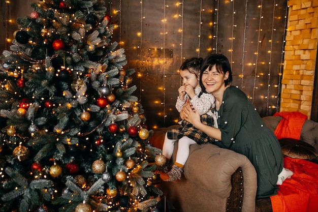 Moeder en dochter zitten naast een kerstboom bij homesmiling