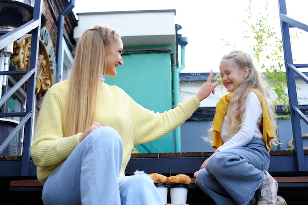 Moeder en dochter zitten op de trappen van het stadscafé en dollen met moeder slaat haar dochter