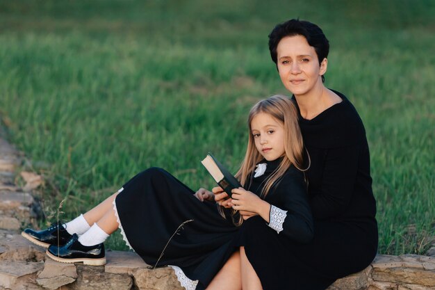 Moeder en dochter zitten op een stenen bank en lezen een boek. Vrouw met een kind in zwarte jurken.