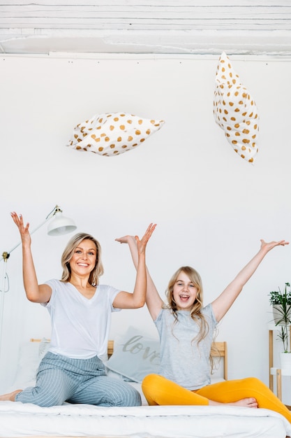 Moeder en dochter zitten op het bed en gooien kussens naar boven, vreugde en plezier, communicatie, familie, stijl, ochtend