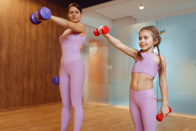 Moeder en dochters doen oefening met halters in de sportschool, fitnesstraining. Moeder en klein meisje in sportkleding, gezamenlijke training in sportclub