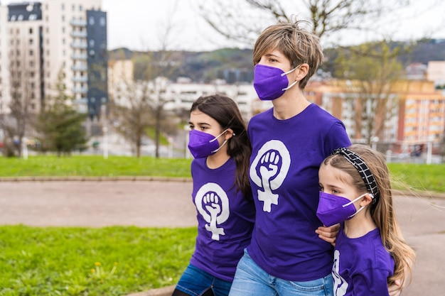 Moeder en dochters lopen over straat en dragen een paars T-shirt met het symbool van werkende vrouwen op Internationale Vrouwendag, 8 maart, en dragen een masker voor de coronavirus-pandemie