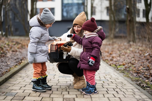 Moeder en dochters met kat in plastic reiskoets buiten in het park