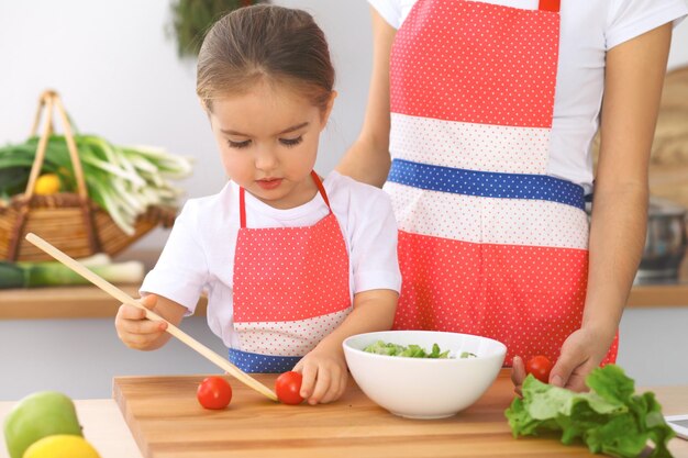 Moeder en dochtertje koken lekker ontbijt van verse salade Kleine helper snijden en mengen van tomaten en groen Concept van gelukkige familie in de keuken of gezonde maaltijd