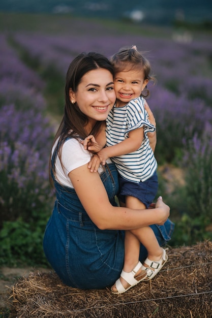 Moeder en dochtertje zitten op hooi bij de boerderij Achtergrond van de zomer lavendelveld Familie denim stijl Klein meisje knuffel moeder