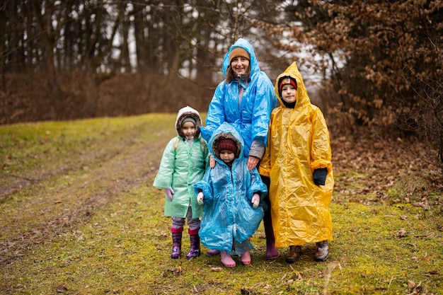 Moeder en drie kinderen samen in het bos na regen in regenjassen