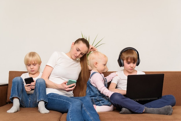 Moeder en drie kinderen zitten op de bank met elk een eigen gadget. probleem van het moderne generatieconcept.