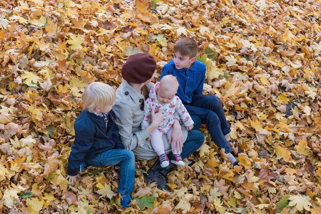 Moeder en drie kinderen zitten op gevallen bladeren in de herfstbos