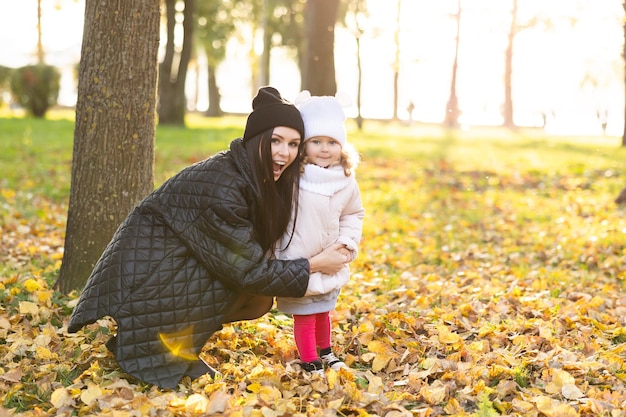 Moeder en een jong meisje met blond haar spelen in een herfstpark op een gele en oranje bladachtergrond Familie loopt in het park