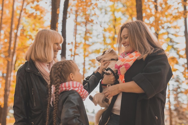 Moeder en grootmoeder en dochter houden jack russell terrier vast en spelen ermee in de herfst buiten p