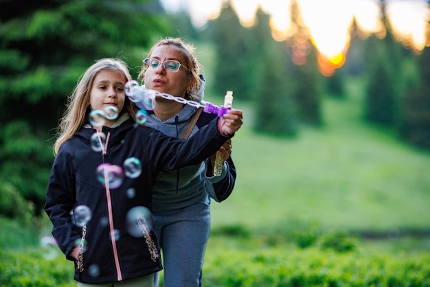 Moeder en haar dochter blazen tijdens een wandeling zeepbellen in het sparrenbos